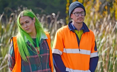 Kylie and Brad in hi vis with weeds behind them.