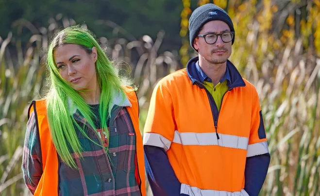 Kylie and Brad in hi vis with weeds behind them.