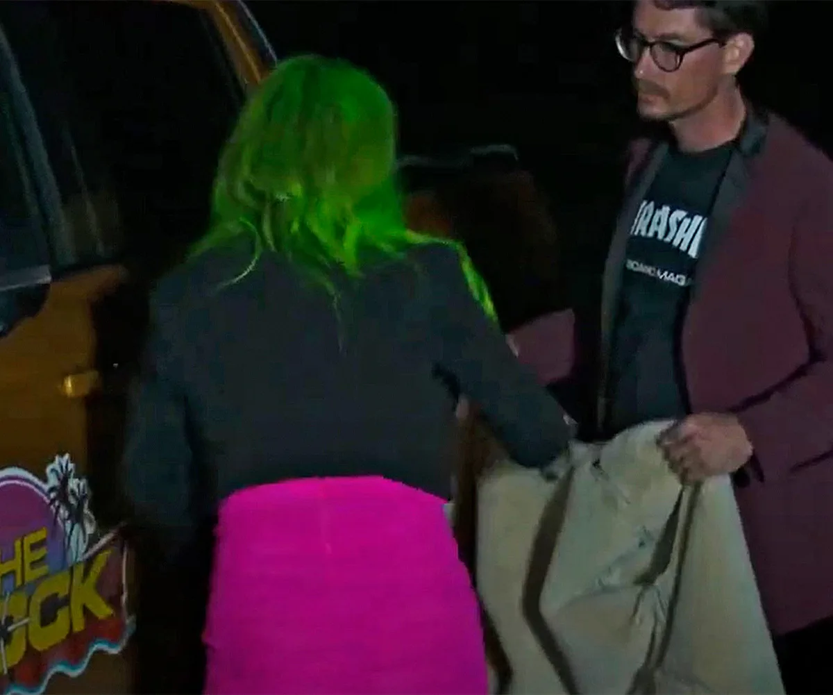 Kylie and Brad leave early in morning, Back of Kylie pictured with green hair, black top, pink jumper around waist with Brad passing her a jacket.