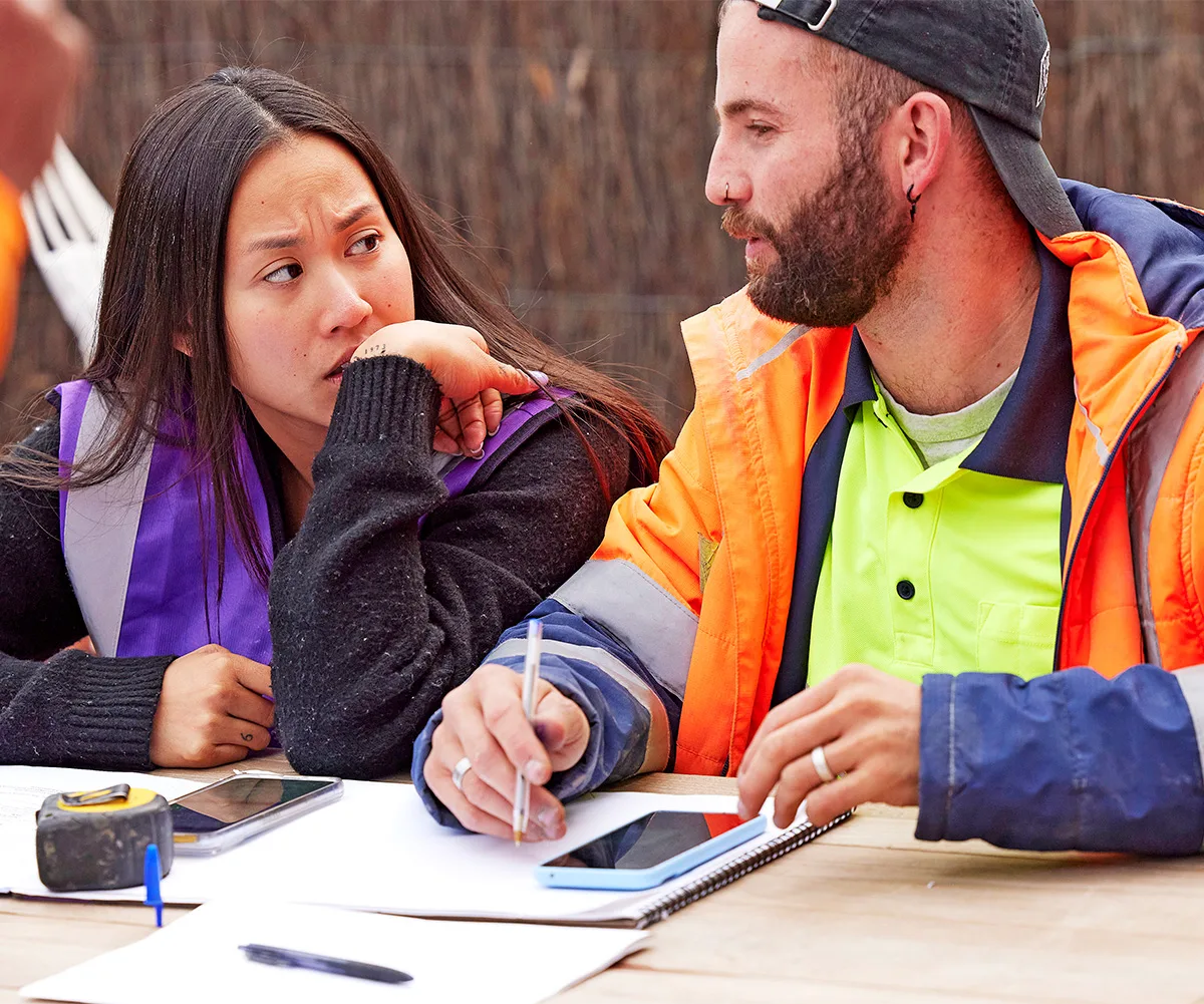 Mimi and Kristian at a desk in hi vis looking stressed