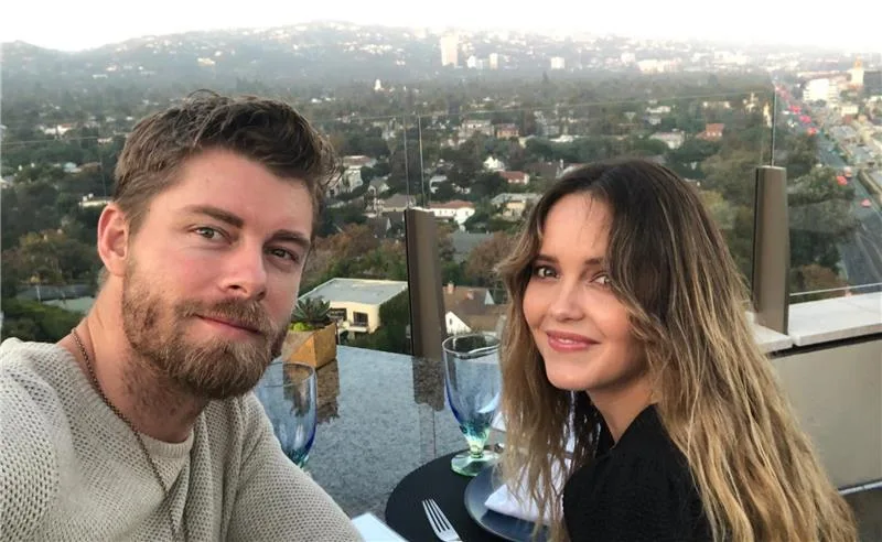 Young couple dining with a scenic city view in the background, sitting at an outdoor table with glassware.