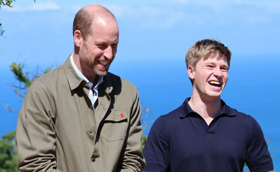 Two people smiling and laughing outdoors with a clear blue sky and ocean in the background.