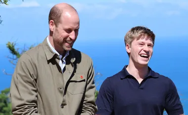 Two people smiling and laughing outdoors with a clear blue sky and ocean in the background.