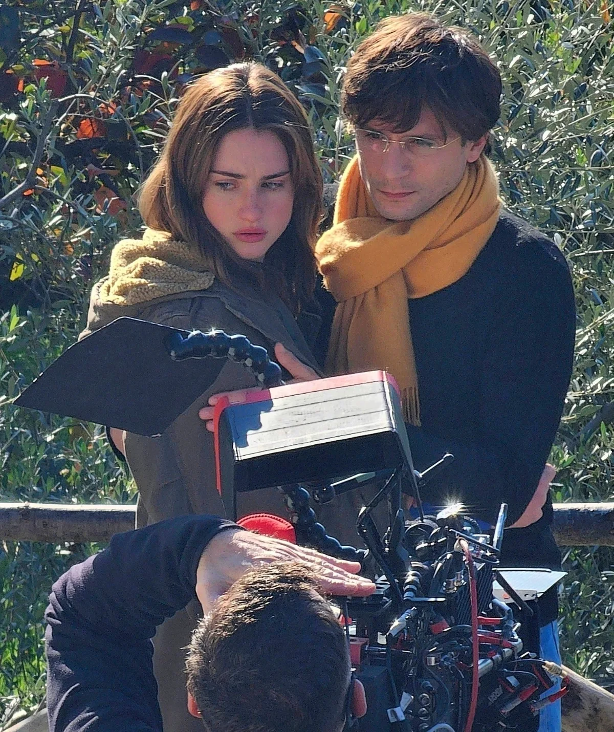 A woman and man, both with brown hair, are looking downcast and there is a film camera in front of them.