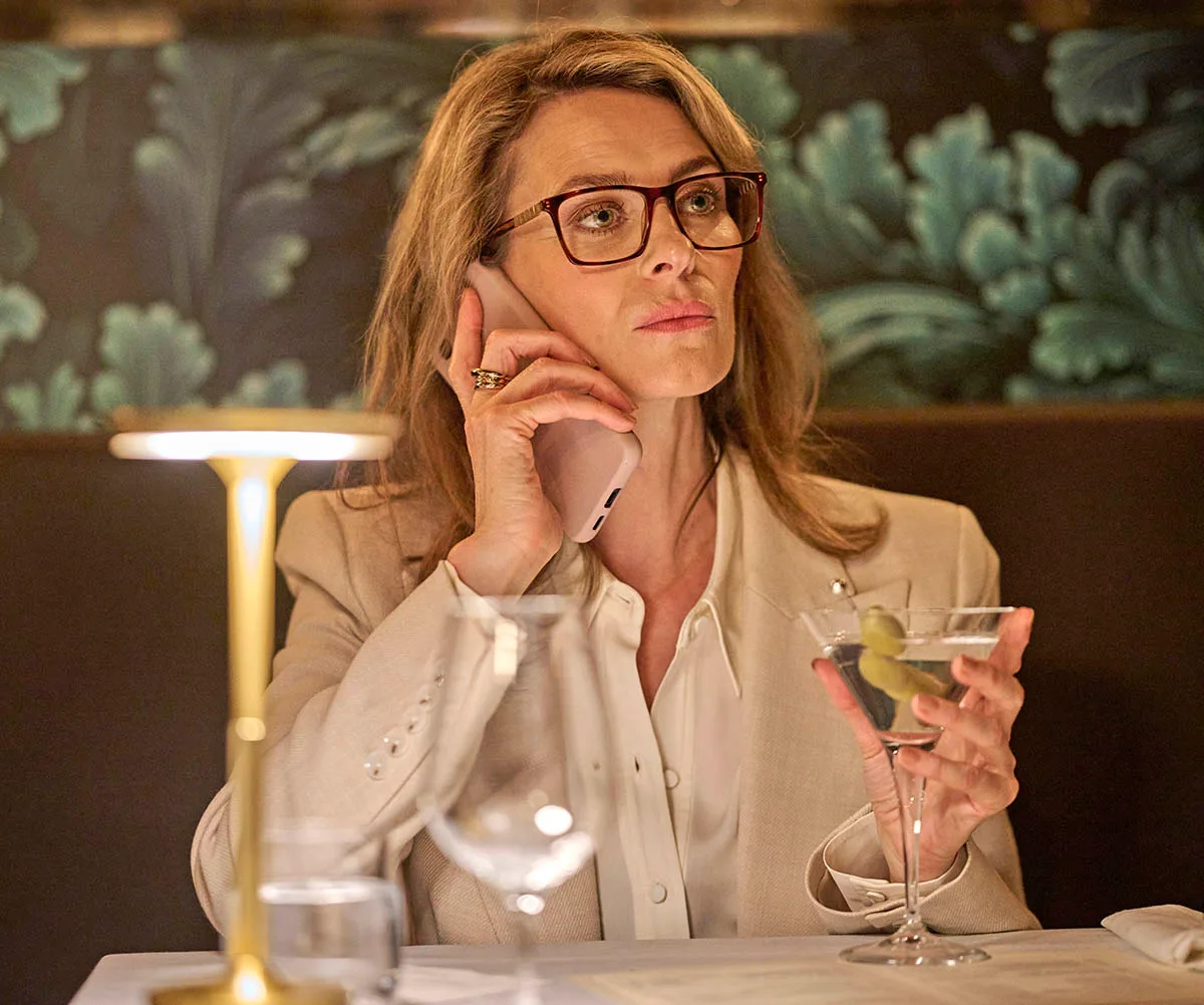 In a still from Black Snow, Kat looks serious as she answers a phone call while sipping on a martini