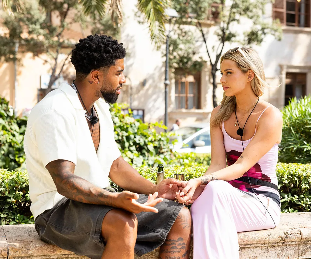 Dylan and Sophie sit facing each other on a ledge in a Spanish square as the talk about their future