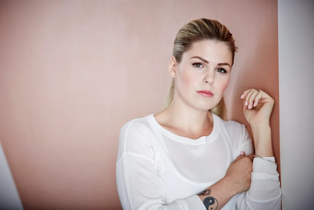 Belle Gibson looking serious in white top on rose pink background
