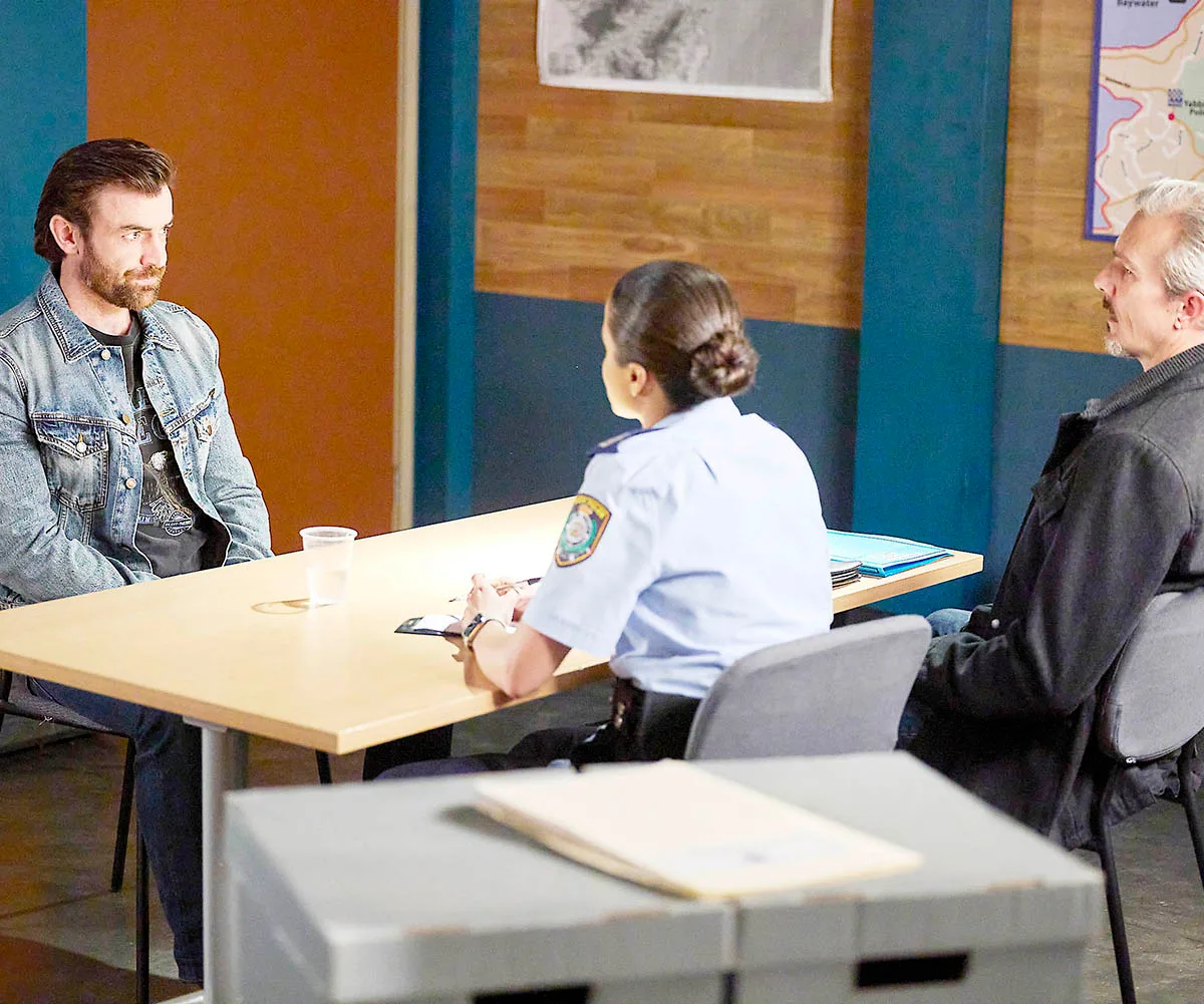 Remi sits at a table with Officer Rose and Detective Townsend as he gives his statement. They sit at a table in the police station.