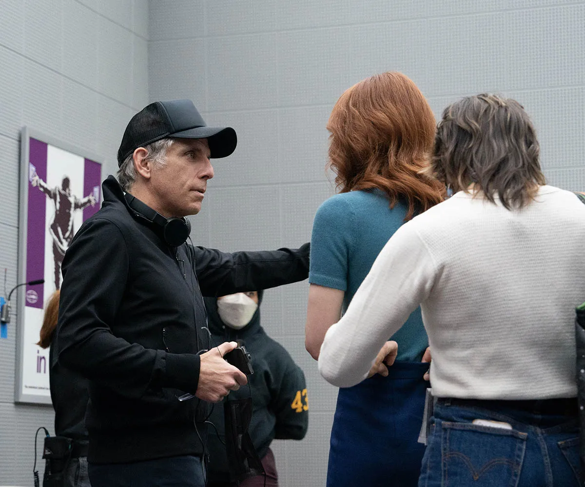 Ben Stiller directing a scene in all black with a hat on. He is showing character Hellie what to do. Someone in a white shirt is in the foreground.