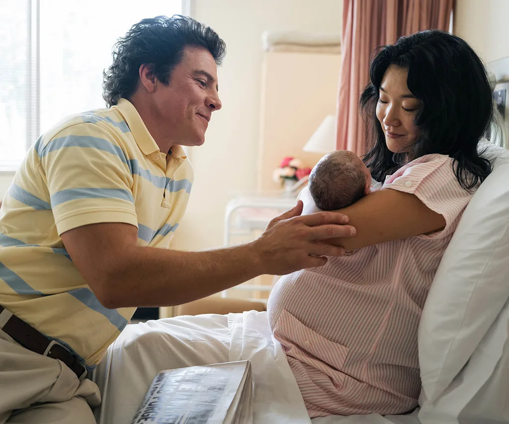 Michelle Lim Davidson, as Noelene, holds her newborn baby in her hospital bed, while Stephen Peacocke, as Rob, looks on, in The Newsreader.
