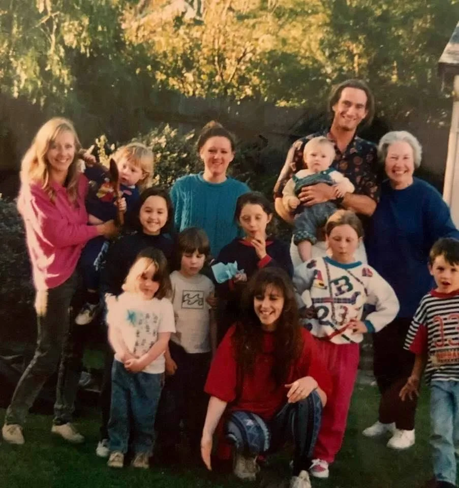 Joan in blue, standing with her extended family, including grandkids, in a park