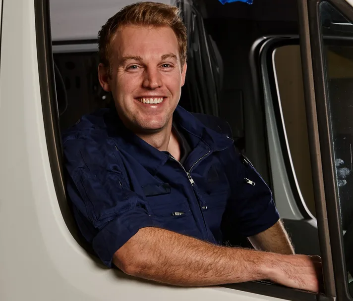 Blond haired man in paramedic uniform smiling as he leans on open ambulance window