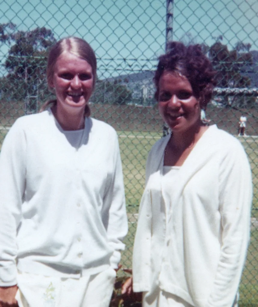 Two women wearing white smile at the camera.