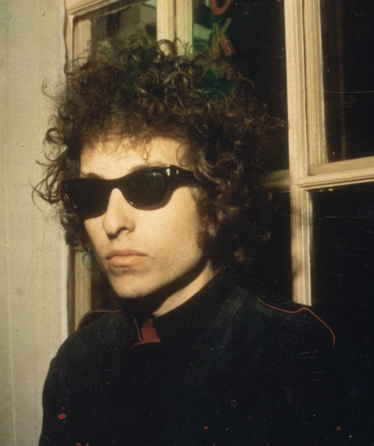 Bob Dylan looks sternly at the camera wearing a pair of wayfarer Ray Ban sunglasses.