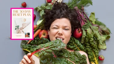 Woman lying on bed of vegetables eating spinach