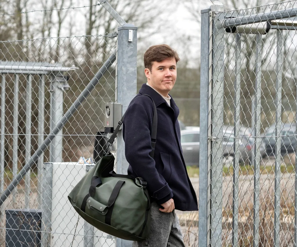 An image of a prince christian looking over his shoulder with a large bag on his arm.