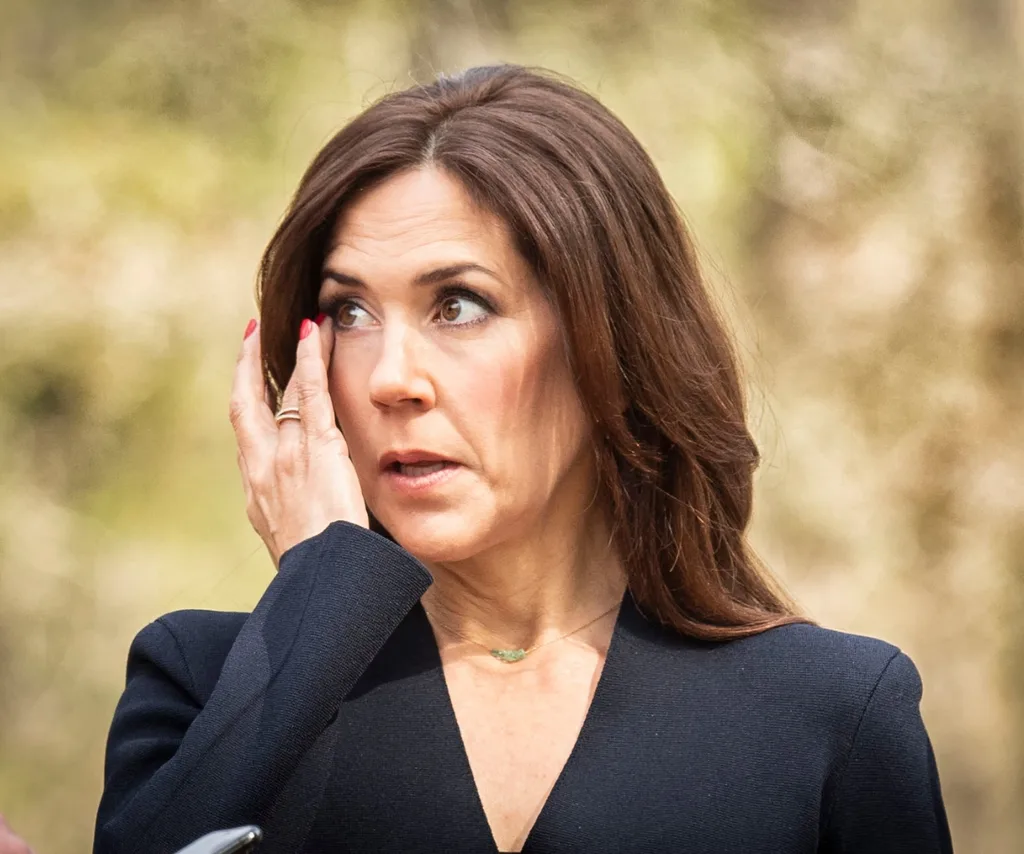 A brown haired woman with her hand up to her face looks to the side.