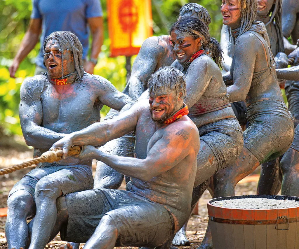 Rich and other team members on Survivor are covered in mud as they compete in a challenge,