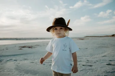 Jaeger Verryt wearing a white t-shirt and brown hat while standing on a scenic beach. (Image: Supplied)