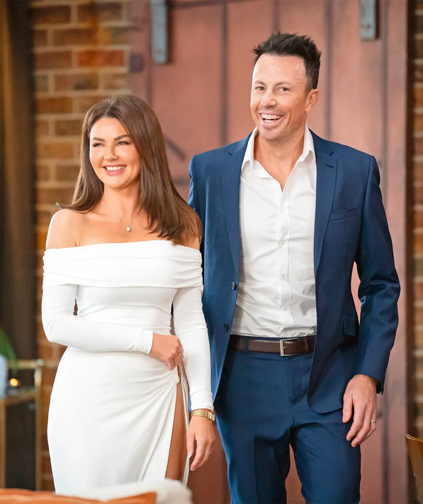 Lauren and Clint walk into the dinner party looking happy. Lauren wears a stunning off the shoulder long sleeve white dress while Clint is in a navy blue suit with a white shirt