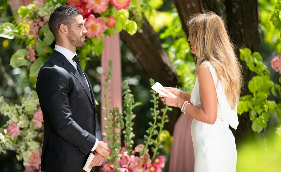 Ryan on the left in a suit with Jacqui on the right in a white dress with a lovely backdrop of greenery and leaves