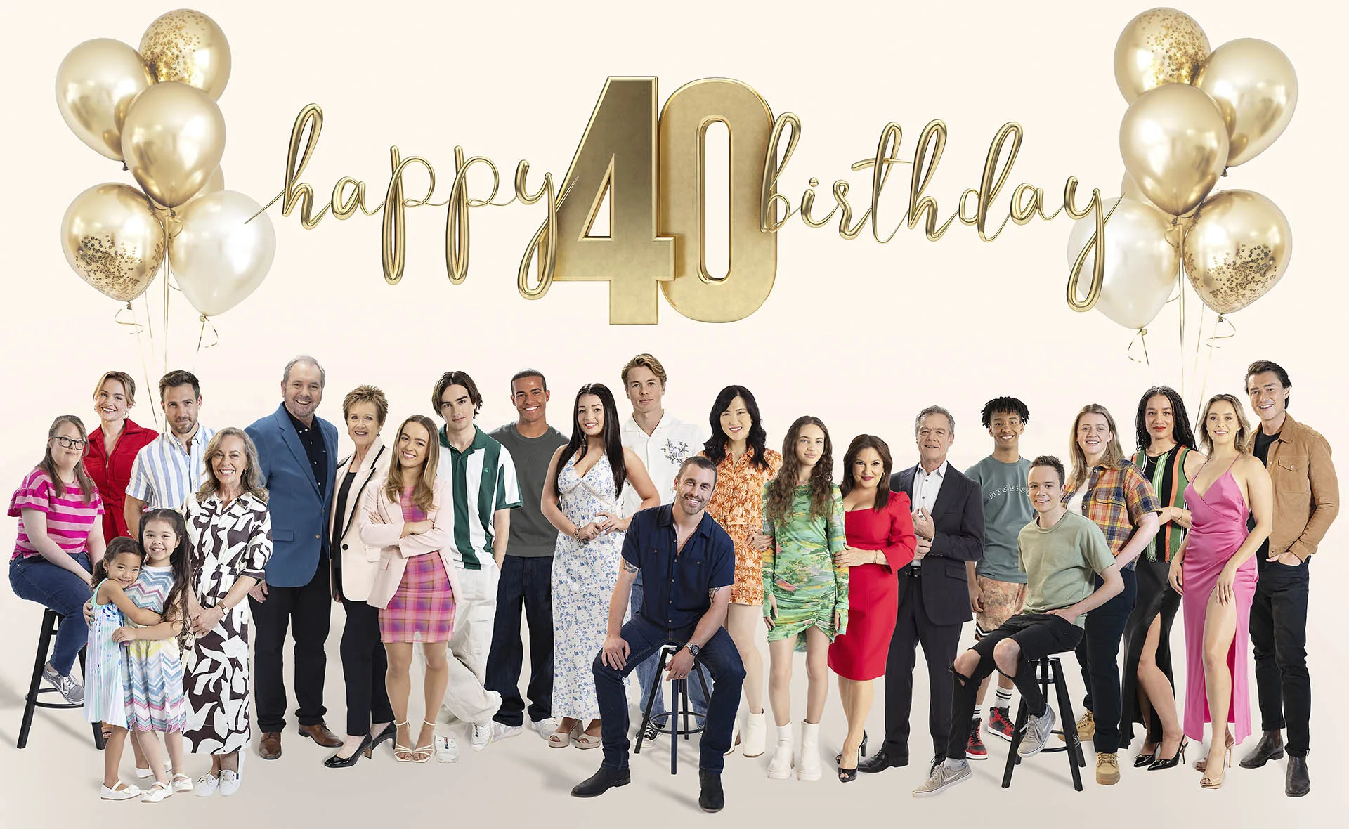 The Neighbours cast gather together for an image to mark 40 years of the series, gold and white balloons are positioned above them with a sign that says Happy 40 Birthday