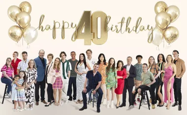 The Neighbours cast gather together for an image to mark 40 years of the series, gold and white balloons are positioned above them with a sign that says Happy 40 Birthday