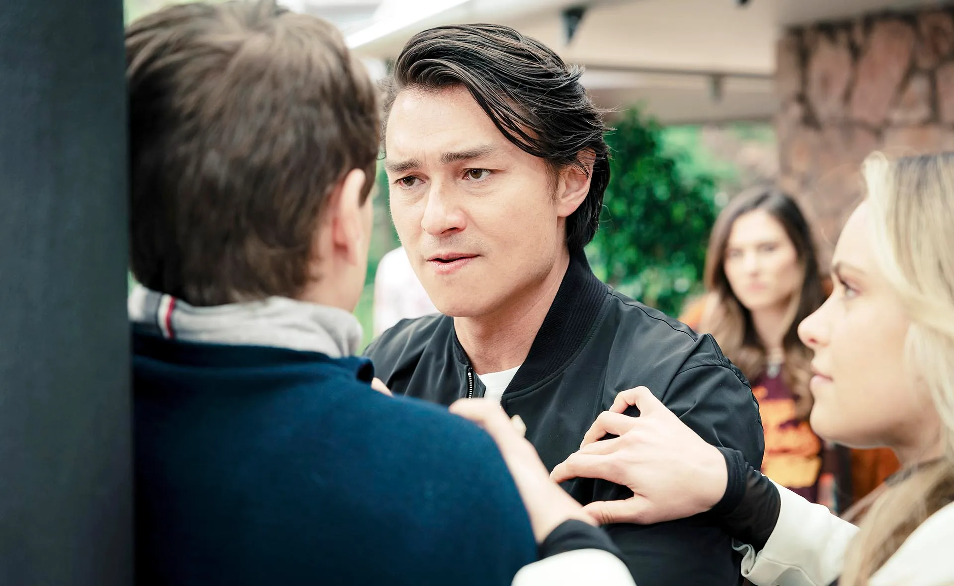 Leo has his hands up against Seb roughing him up as Krista tries to separate them and Fallon watches on in the background