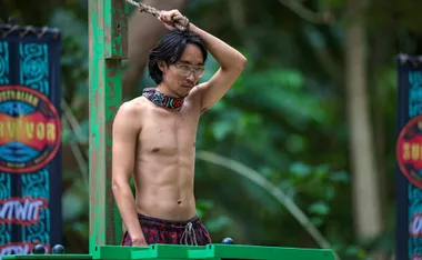 Myles, with his shirt off and his buff around his neck, is holding onto a rope with one hand, as part of a challenge on Australian Survivor.