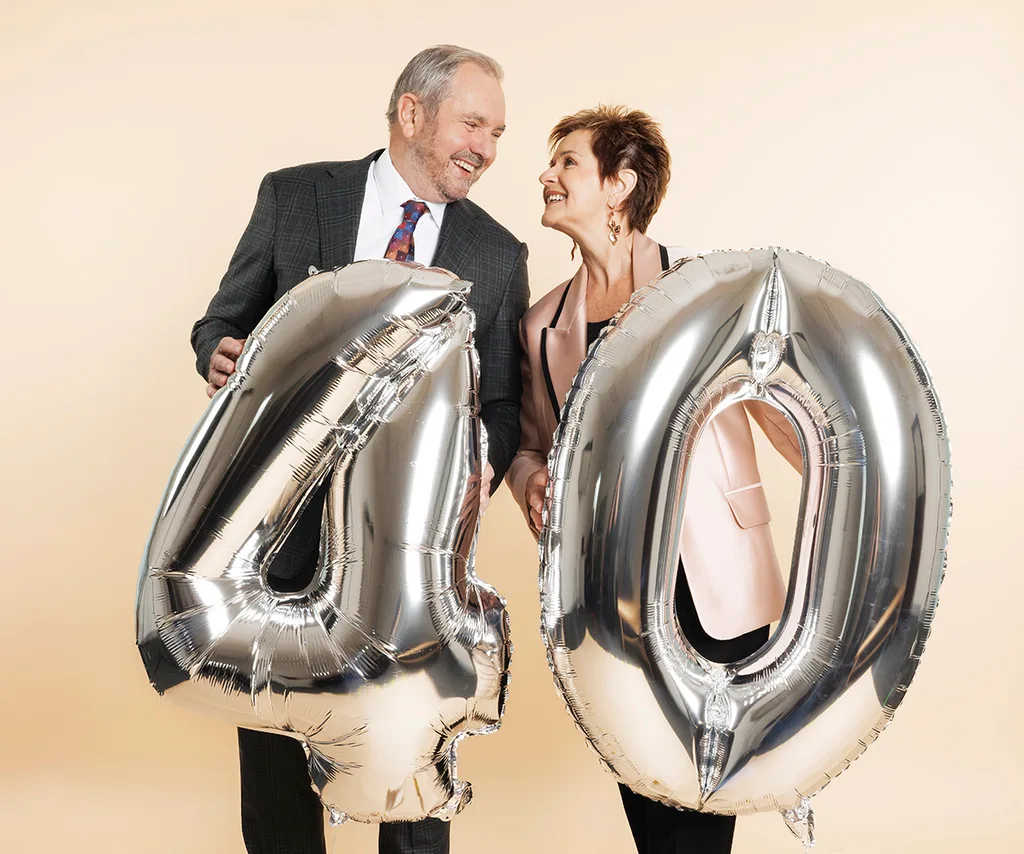 Alan Fletcher and Jackie Woodburne pictured with two big balloons that say 40 on a beige background.