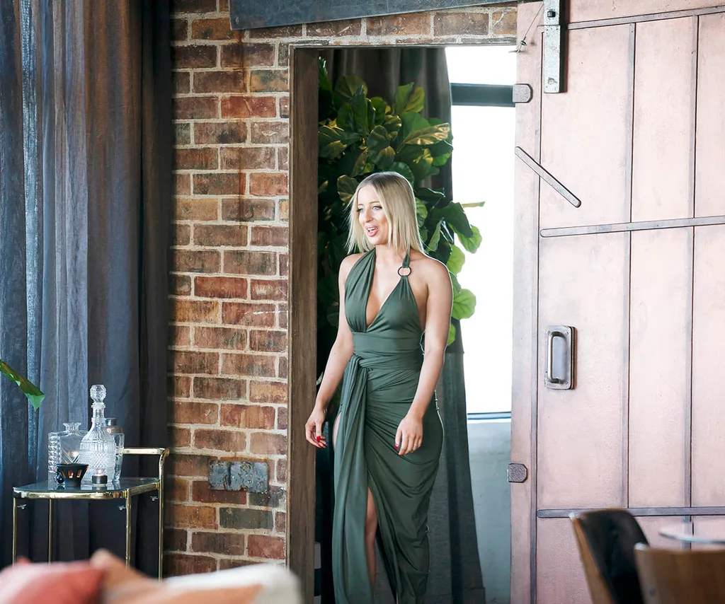 Jamie, wearing a long olive dress, walks into the dinner party