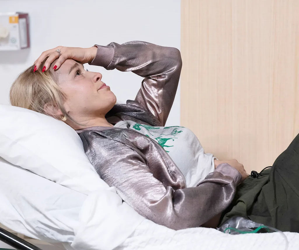 Roxy Canning lays in a hospital bed with her hand on her head looking like she is about to cry