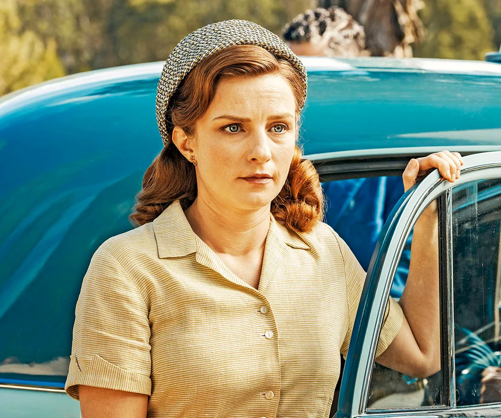 Faye Marsay, as Annie, wearing a scarf on her head and a beige shirt, gets out of a blue car.
