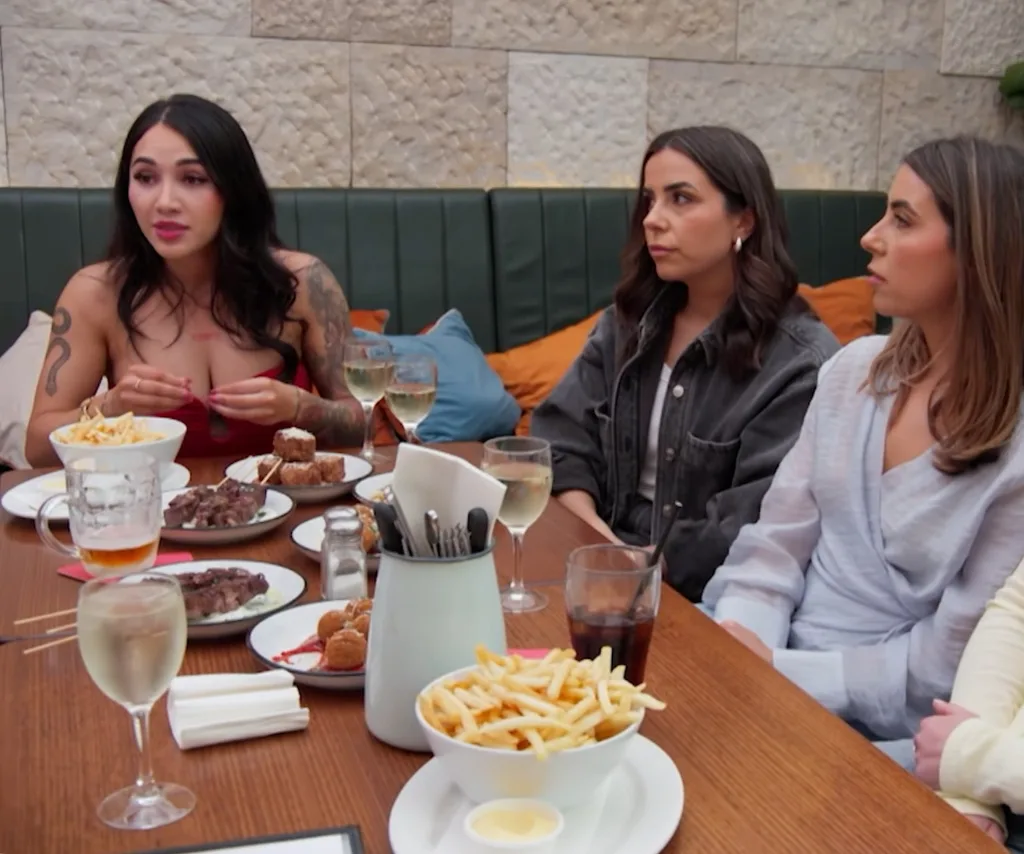 Cleo sits at a table with Adrian's twin sisters