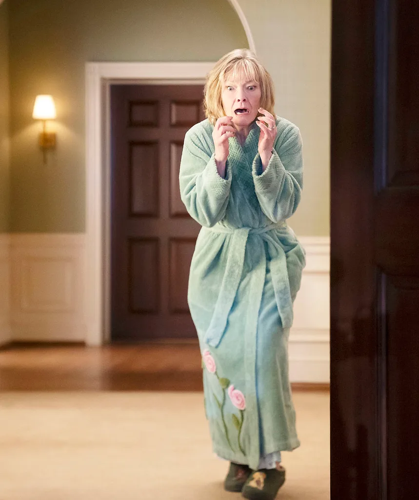 Jane Curtin, as Nan, wearing a dressing gown, stands in a room with a shocked look on her face.