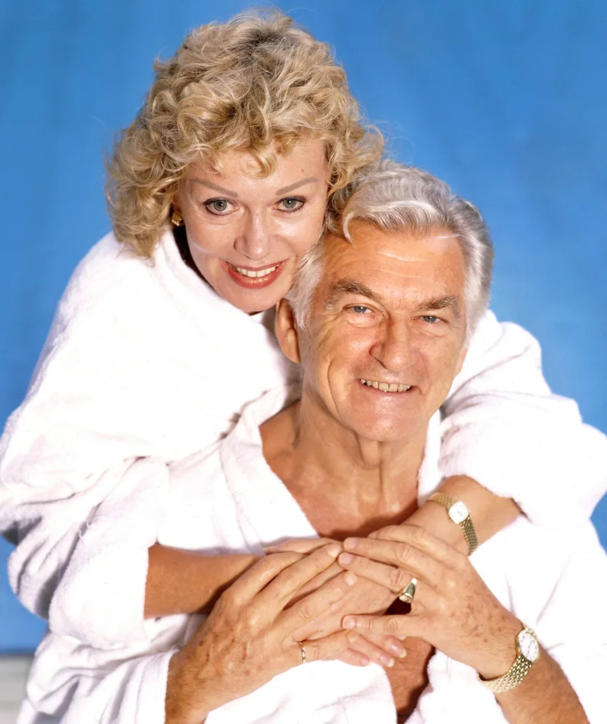 Blanche and Bob pose in white towel robes in front of a blue backdrop.
