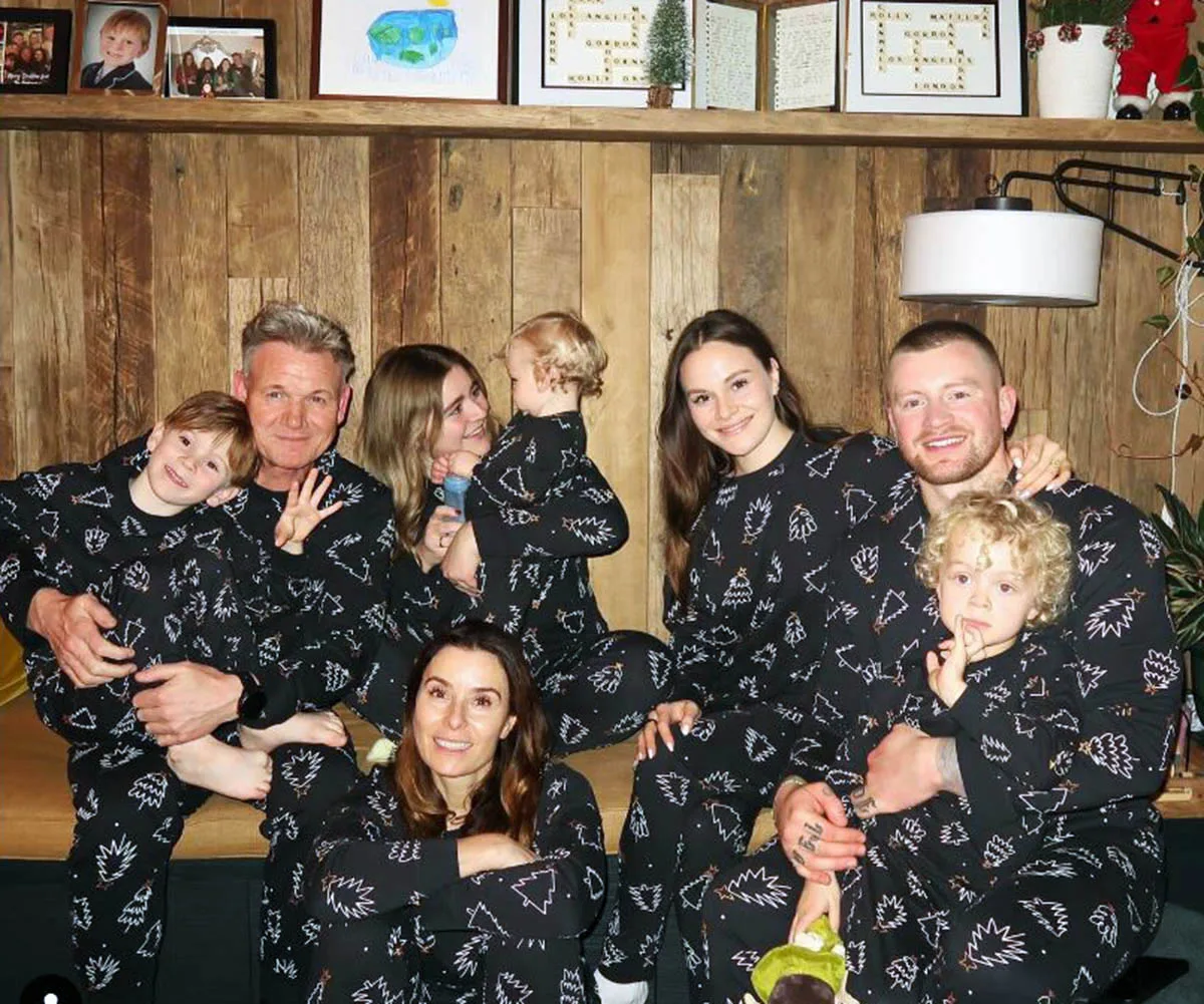 Gordon is pictured in front of a wooden wall in black matching pyjamas that have Christmas trees on them with his wife and six kids 