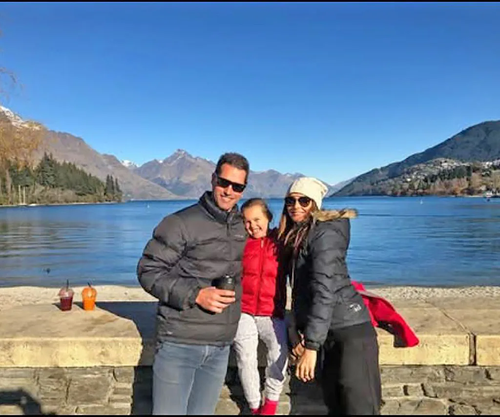 Nat and her family are dressed for cooler weather in front of a lake with mountains in the background