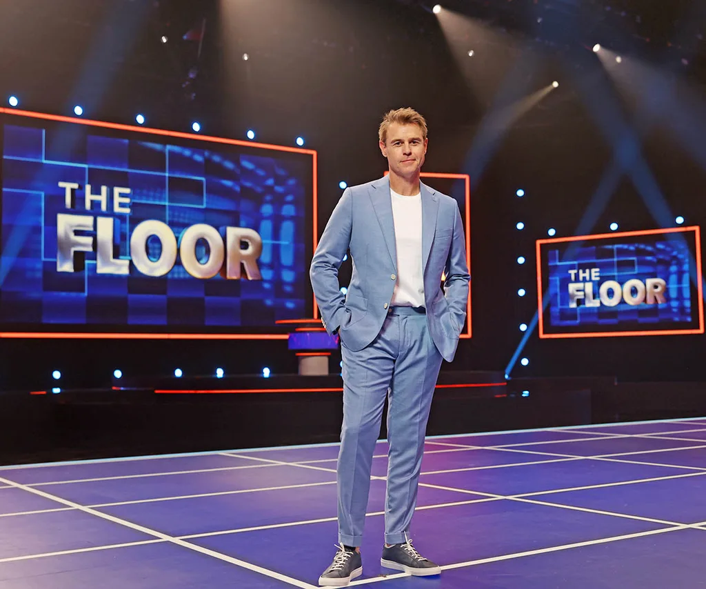 Rodger Corser stands in a blue suit with white t-shirt on The Floor stage