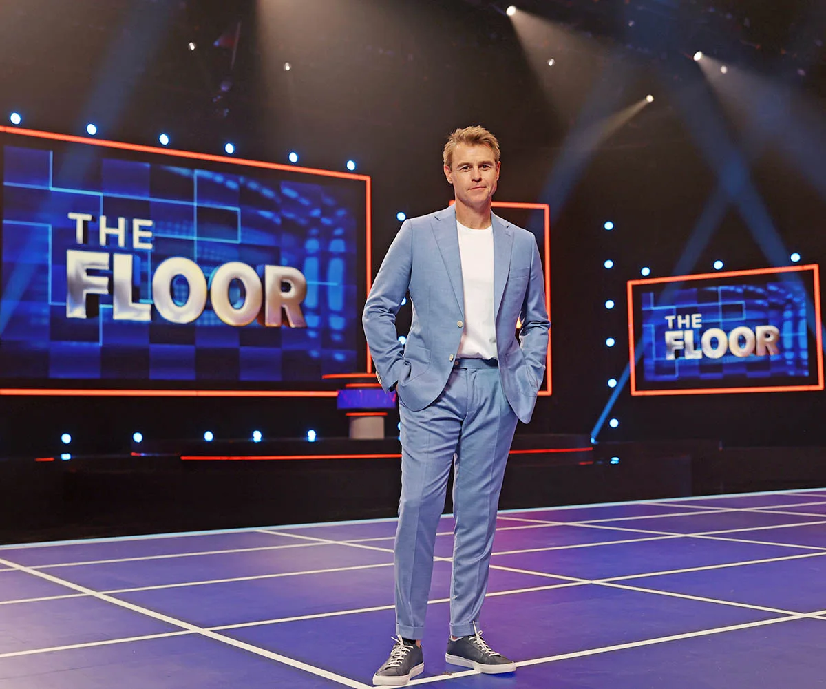 Rodger Corser stands in a blue suit with white t-shirt on The Floor stage