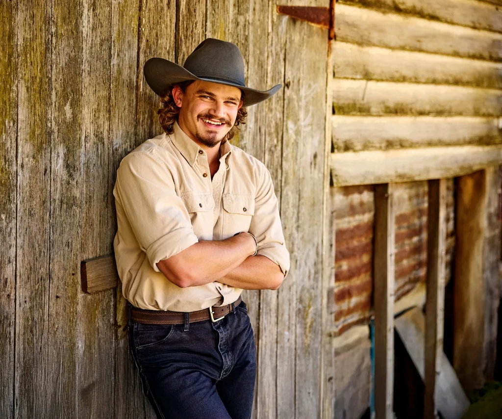 Farmer Jarrad leans against a wooden fence in a promo still for Farmer Wants A Wife