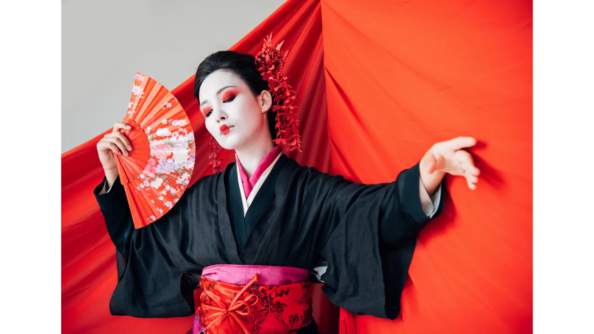 A Japanese geisha poses artfully with a fan dressed in a black kimono.