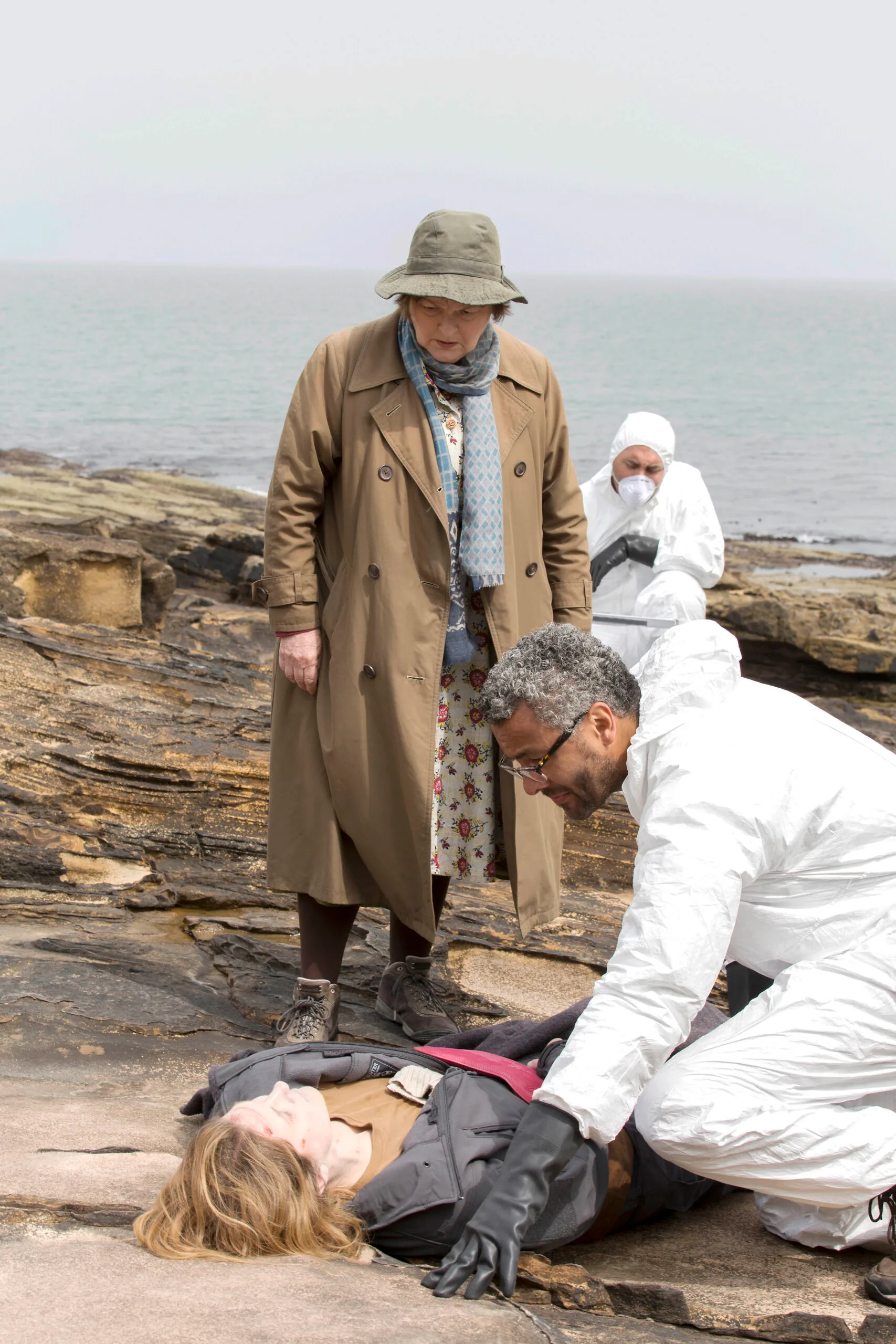 Vera looks over the body of a young girl on the rocks near a beach while detectives in white hazmat style suits work around her obtaining clues