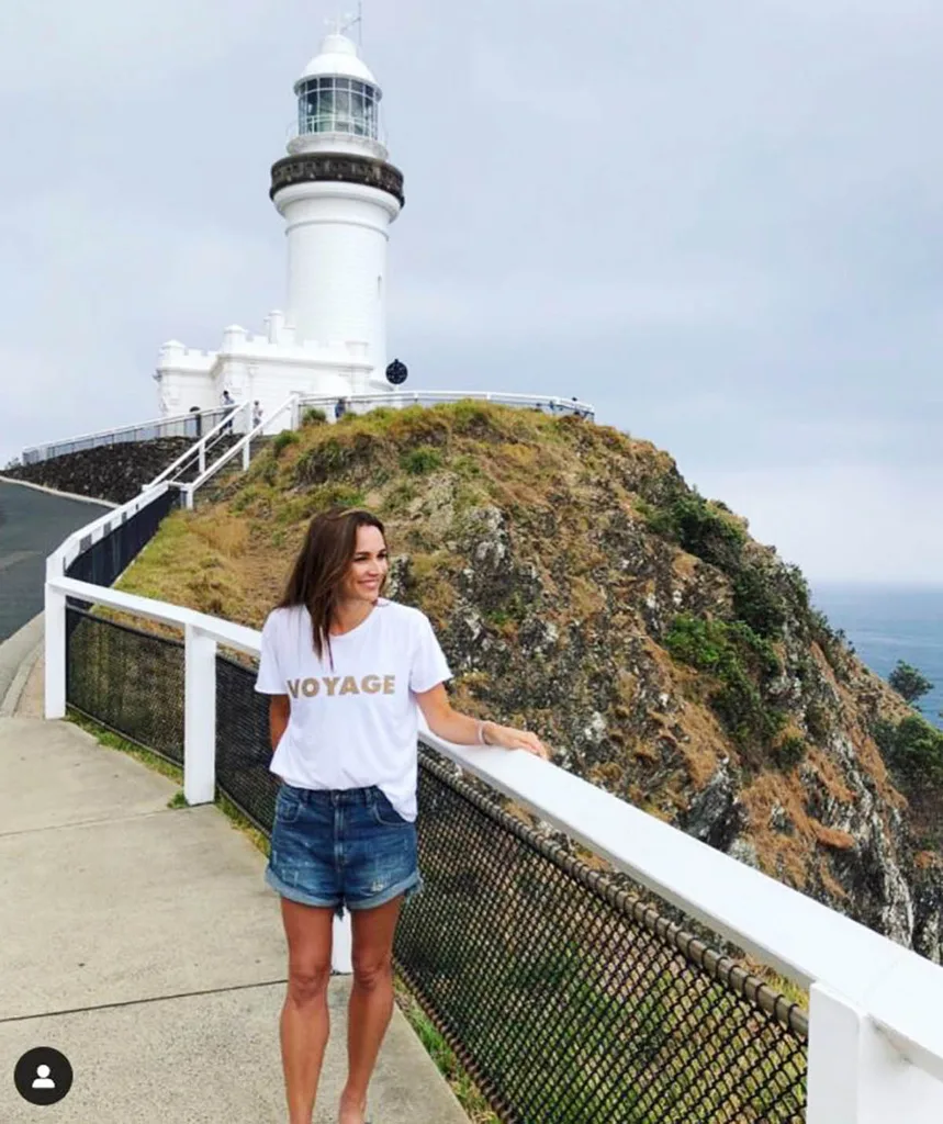 Nat pictured in a white tee and shorts in front of the famous lighthouse in Byron Bay, NSW
