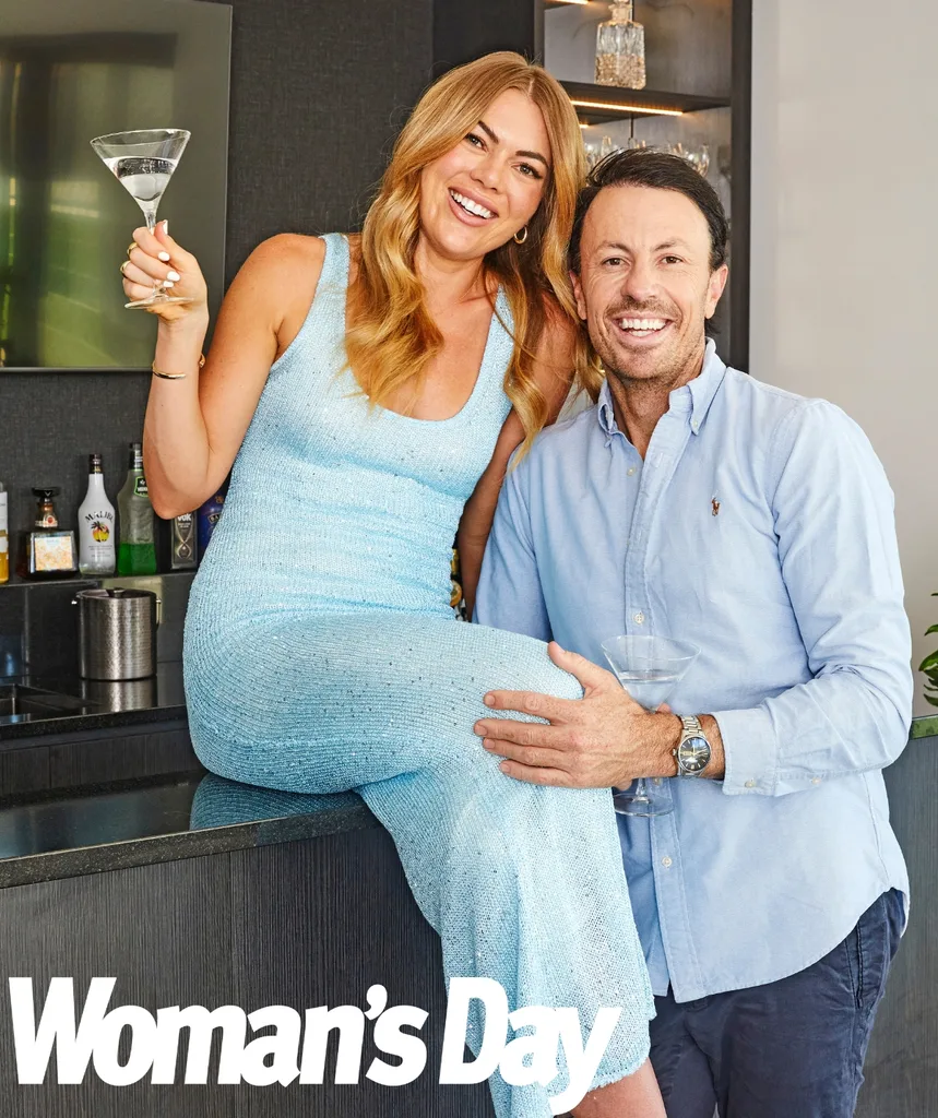 Jacqui sits on the bar with a martini glass while Clint stands next to her