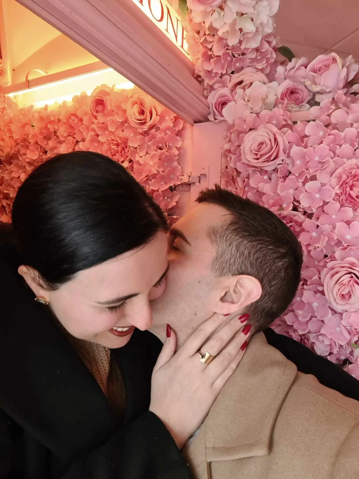 Elinor and Daniel kissing in front of a wall of pink roses