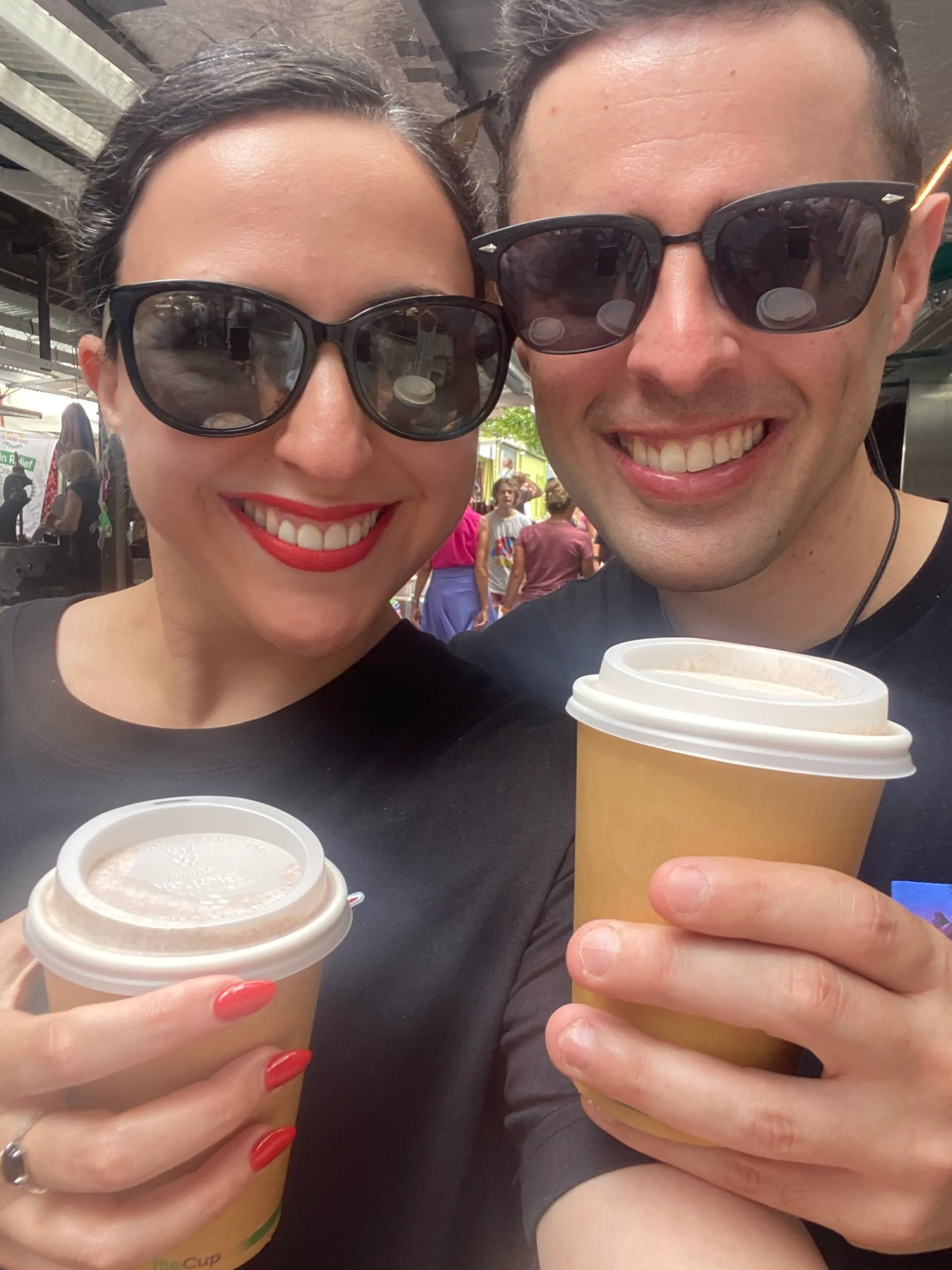 Elinor and Daniel wearing sunglasses and holding coffee cups