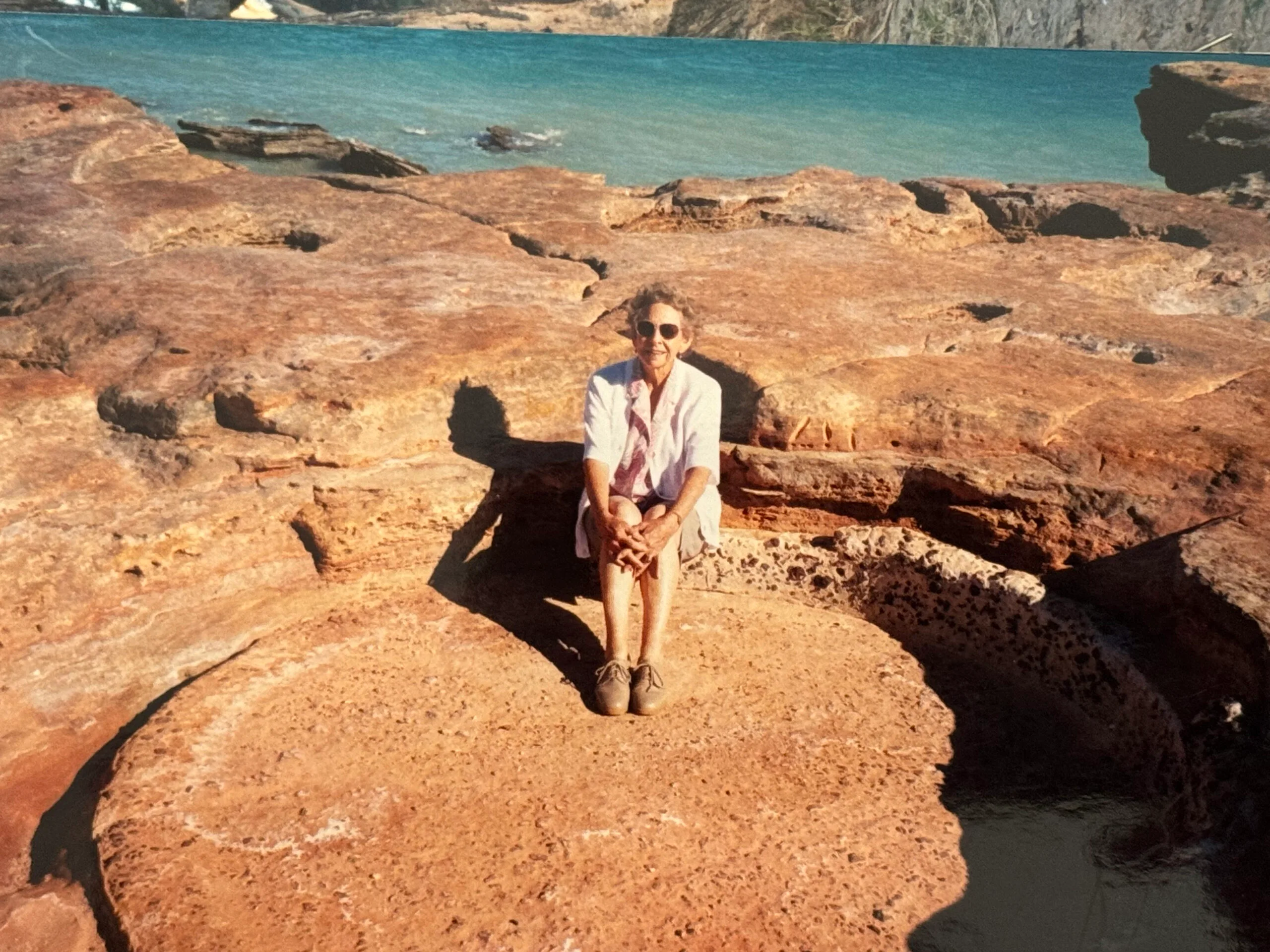 Bonnie sitting on red, beachside rocks in WA in the '80s