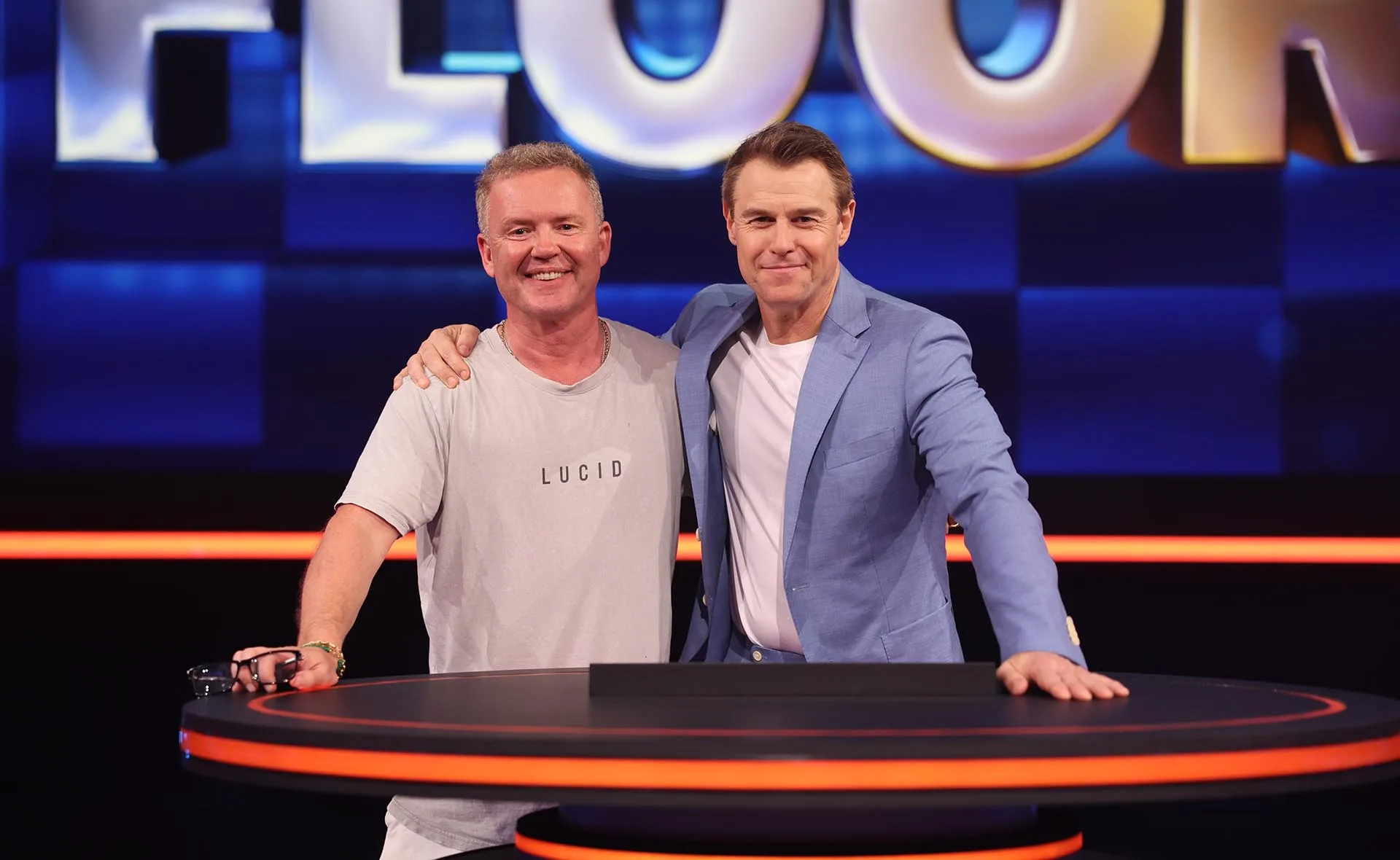 Andrew Peace in a grey t shirt hugging Rodger Corser on set of The Floor