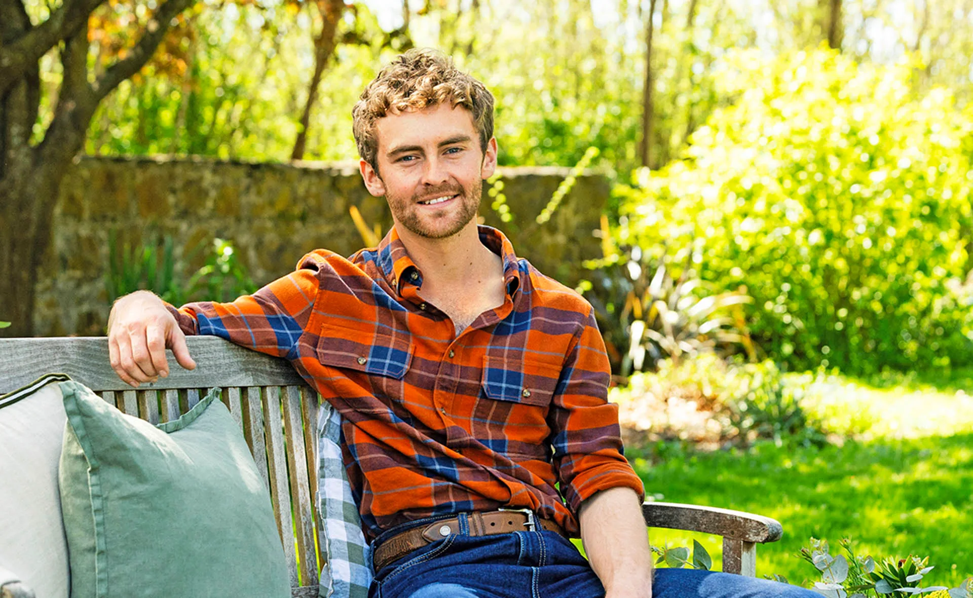 Farmer Jack, wearing a red checked shirt, sits in a garden on a bench.